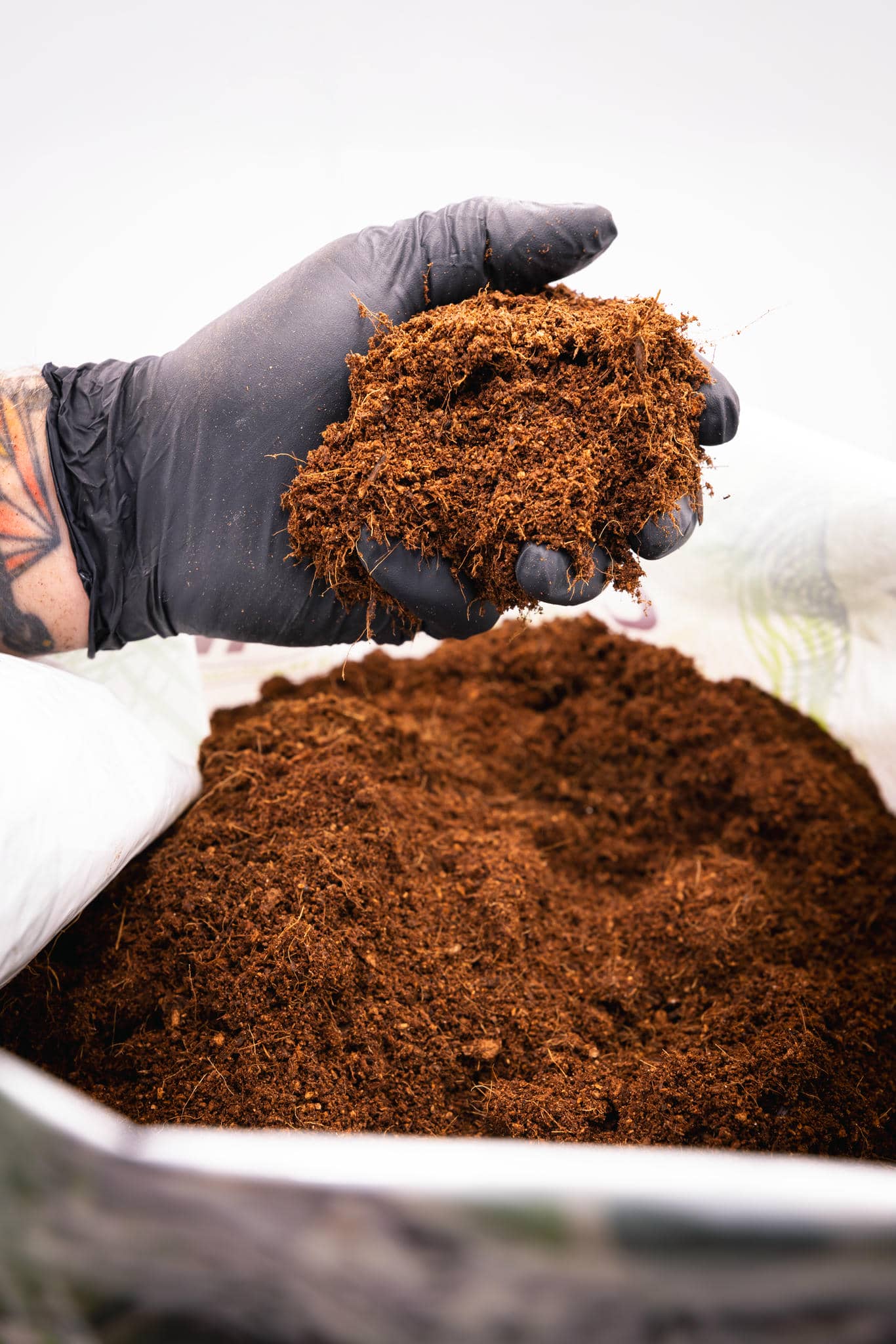 Hand with glove holding Coconut Coir from bag of Coir